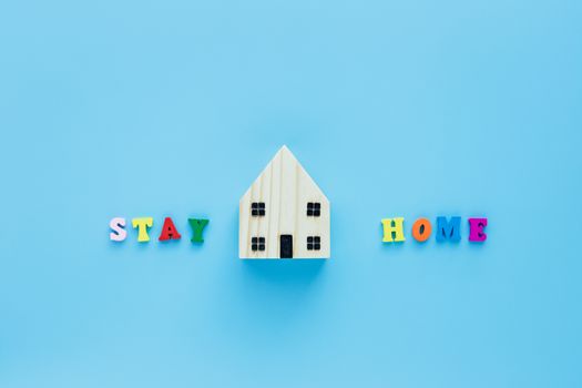 Stay home text with wooden house model on blue background for self-quarantine, staying home and social distancing in coronavirus or Covid-2019 situation concept