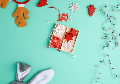 burning christmas garland on a white wire with colorful lights and box with wooden toys for the Christmas tree on a green background, copy space