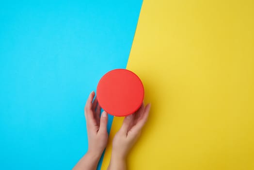 two female hands hold a closed paper cardboard box on a yellow-blue background, concept of surprise