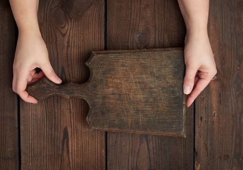 two hands holding a vintage brown empty kitchen cutting board with a handle over a table from the boards, top view