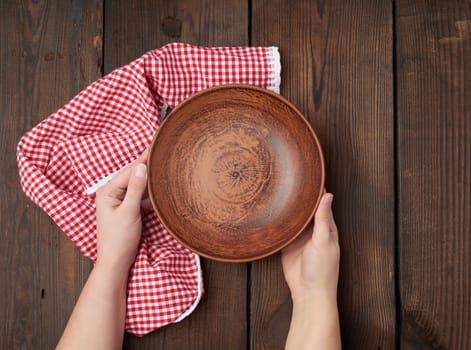 two female hands holding an empty round clay plate, top view