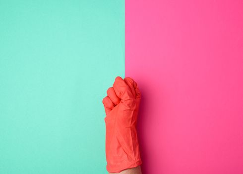 hand in a rubber orange glove for cleaning a house clenched into a fist on a colored background, the concept of gender equality