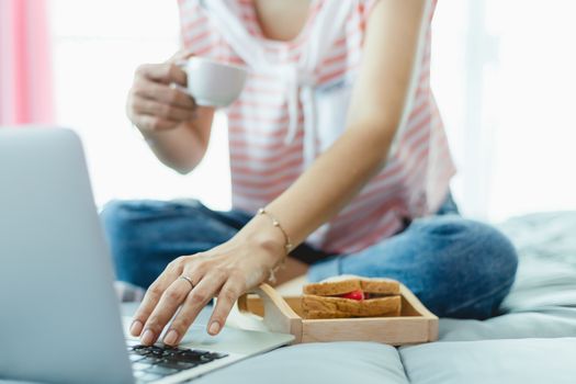 Woman using computer and having breakfast in bed for self-quarantine, social distancing, staying and working at home in coronavirus or Covid-2019 outbreak situation concept