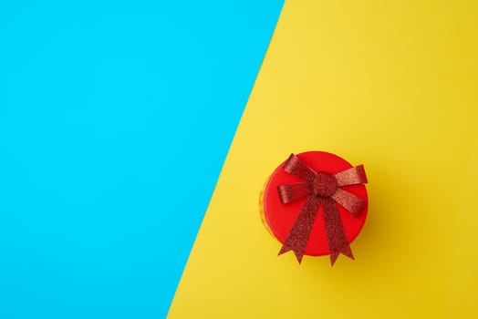 round cardboard red box with a bow on a blue-yellow background, top view, place for text