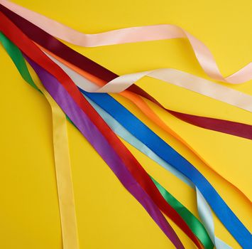 many silk multi-colored ribbons on a yellow background, top view