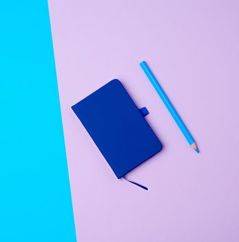 closed notebook and wooden blue pencil on a colored background, top view, flat lay