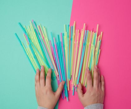 female hand holding multicolored plastic cocktail tubes, green pink background