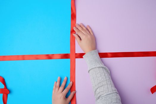 two female hands tie a bow with a satin red ribbon on a gift box, top view
