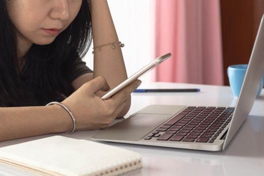 Woman using smartphone with computer laptop and working at home for business, self-quarantine, staying home and social distancing in coronavirus or Covid-2019 outbreak situation concept