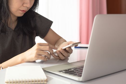 Woman using smartphone with computer laptop and working at home for business, self-quarantine, staying home and social distancing in coronavirus or Covid-2019 outbreak situation concept