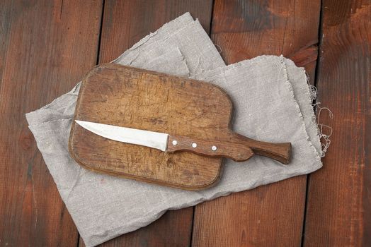 very old empty wooden rectangular cutting board and knife, top view, brown wooden background 
