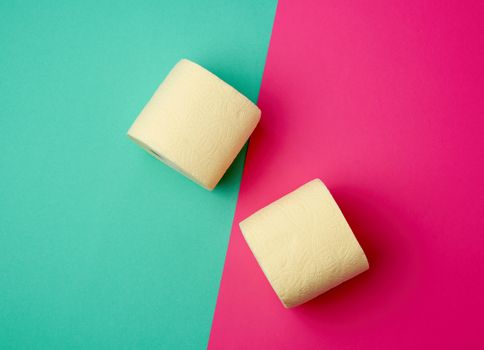 soft yellow toilet paper in a roll on a green-pink background, top view