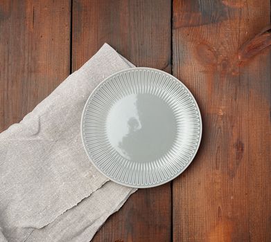 empty gray round ceramic plate stands on a linen napkin, wooden background, top view