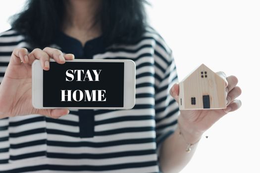 Woman's hand holding smartphone and wooden house model with alert notification for self-quarantine, staying home and social distancing in coronavirus or Covid-2019 outbreak situation concept