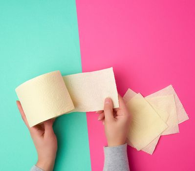 roll of yellow toilet paper in female hands, torn pieces on a colored background, top view