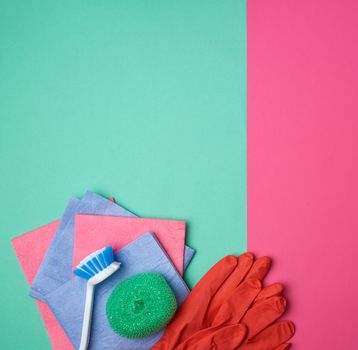 items for home cleaning: red rubber gloves, brush, multi-colored sponges for dusting on a pink green background, top view, flat lay