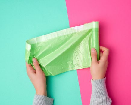 female hand unwinds a green plastic bag for rubbish, green pink background