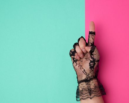 hand in a black lace glove on a pink-green background, top view, finger raised up