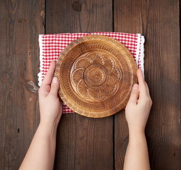 two female hands holding an empty round wooden plate, top view