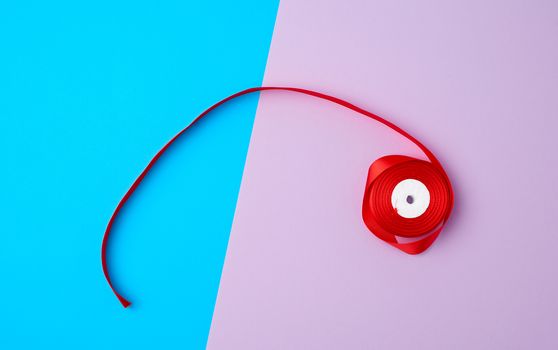 spools with red satin ribbon on a color background, top view