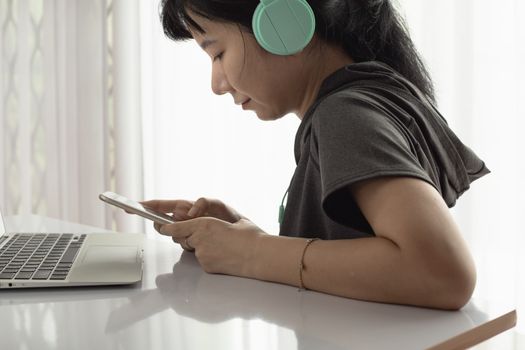 Woman wearing headphones, using smartphone with laptop and staying at home for self-quarantine, staying home and social distancing in coronavirus or Covid-2019 outbreak situation