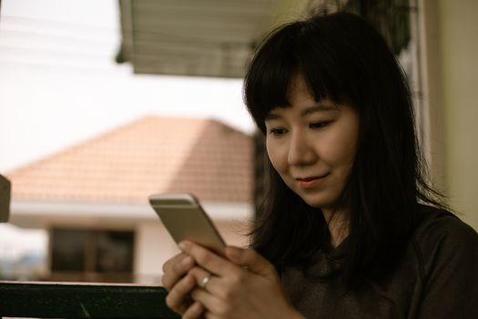 Asian woman using smartphone and staying home for self-quarantine and social distancing in coronavirus or Covid-2019 outbreak situation concept