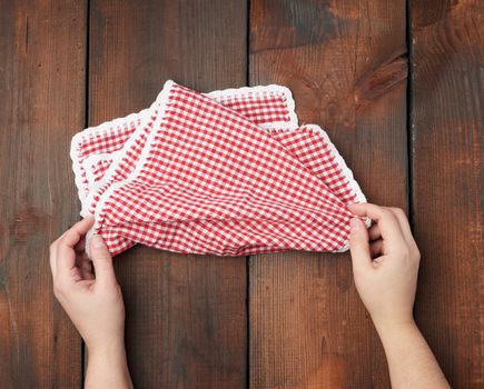 hands hold white red checkered kitchen towel on a brown wooden background, picnic background, top view