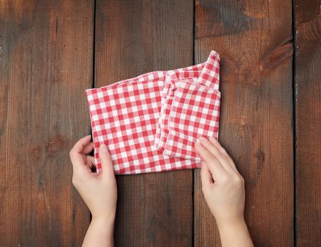 hands hold white red checkered kitchen towel on a brown wooden background, picnic background, top view