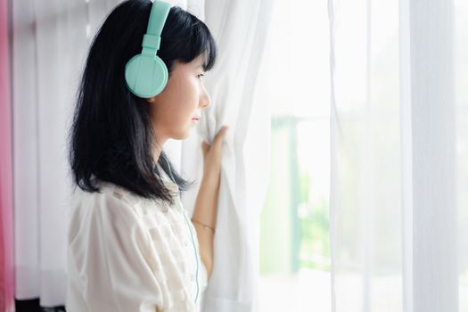 Asian woman staying home, wearing headphones and standing absent-minded at the door for self-quarantine and social distancing in coronavirus or Covid-2019 outbreak situation concept