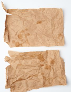 torn crumpled pieces of brown paper with grease stains on a white background, top view