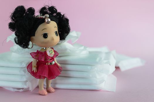 Lady doll with feminine sanitary napkin, an absorbent item worn by a woman while menstruating on pink background for hygiene and health concept