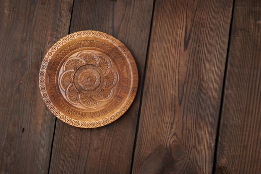 empty round brown carved decorative plate standing on a wooden background from old boards, top view