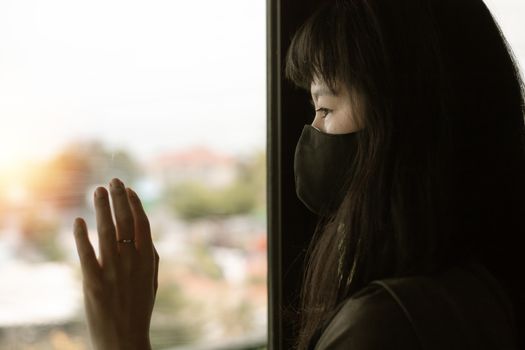 Asian woman wearing a black face mask, standing absent-minded at the door and staying home for self-quarantine and social distancing in coronavirus or Covid-2019 outbreak situation concept