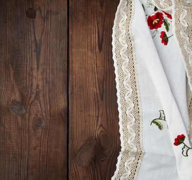 embroidered white dishcloth with lace on a brown wooden background, place for text 
