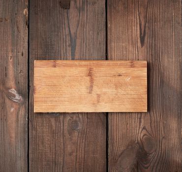 very old empty wooden rectangular cutting board, top view, brown wooden background 