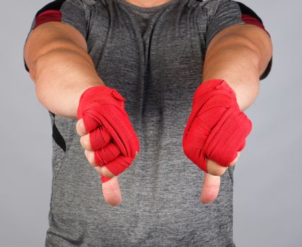 adult athlete in gray uniform and hands rewound with textile red bandage shows gesture dislike, white background 