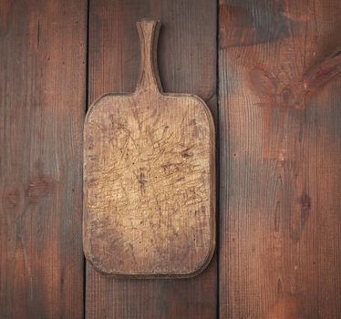 very old empty wooden rectangular cutting board, top view, brown wooden background 