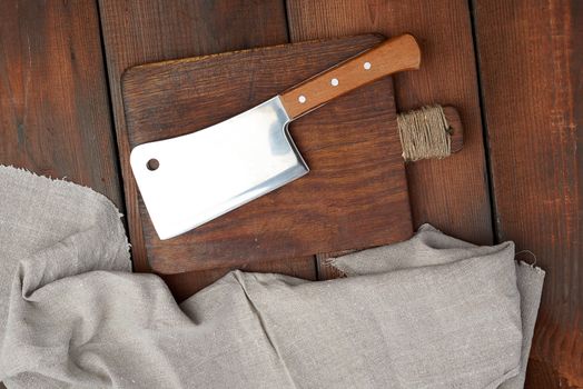 large steel sharp meat knife lies on a rectangular wooden brown board, top view