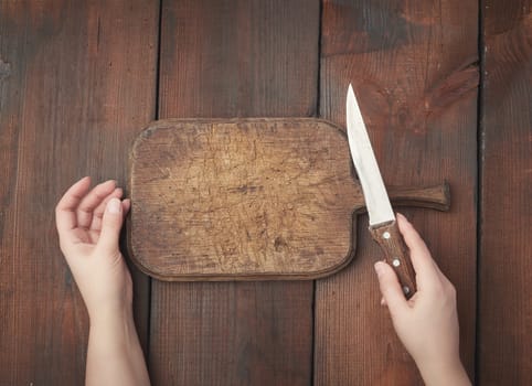 very old empty wooden rectangular cutting board and hands hold a sharp knife, top view, brown wooden background 