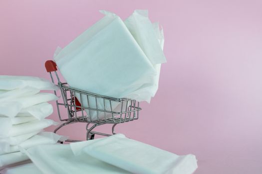 Feminine sanitary napkin, an absorbent item worn by a woman while menstruating, with shopping cart on pink background for hygiene and health concept