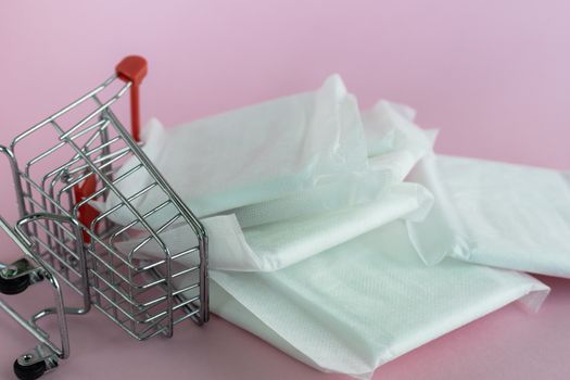 Feminine sanitary napkin, an absorbent item worn by a woman while menstruating, with shopping cart on pink background for hygiene and health concept