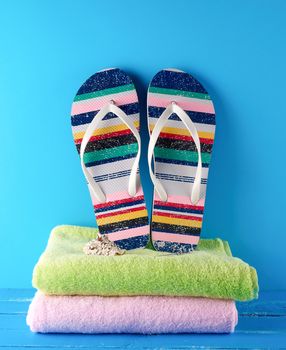 pair of female beach slippers and a towels on a blue background, concept of a vacation at sea