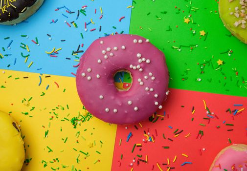 round different donuts with sprinkles on a bright multi-colored background, top view