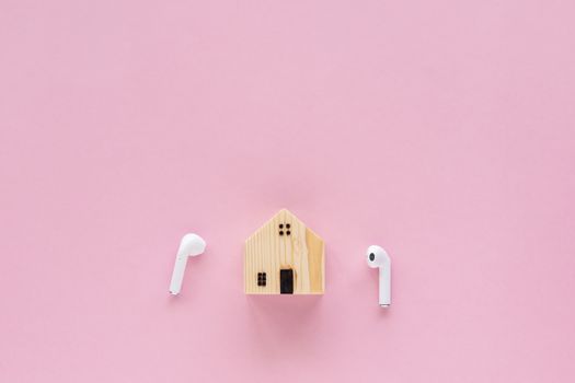 Wooden house model with wireless headphones on pink background with copy space for time to relax,  self-quarantine, staying home and social distancing in coronavirus or Covid-19 outbreak situation