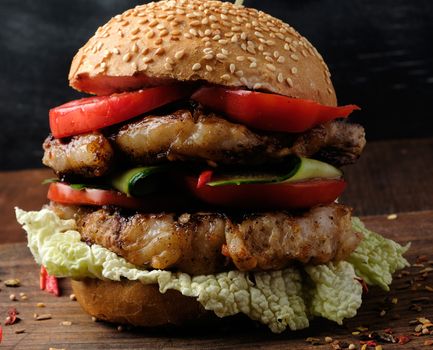 hamburger with pork fried steak, red tomatoes, fresh round bun with sesame seeds on a vintage brown wooden board