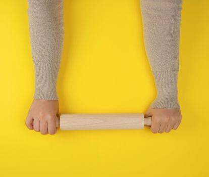 hand holding a wooden rolling pin on a yellow background, top view