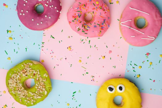whole round pink donuts with colored sprinkles lie on a blue-pink background, top view, pastel colors