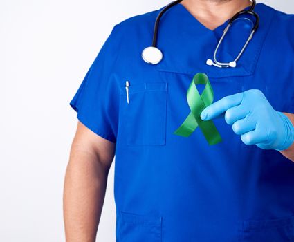 doctor in blue uniform and latex gloves holds a green ribbon as a symbol of early research and disease control, symbol of Lyme disease, kidney transplantation and organ donation