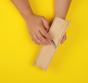 wooden grater for vegetables in hands on a yellow background, top view