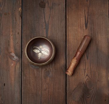 singing Tibetan copper bowl and wooden stick on a table of brown boards, top view